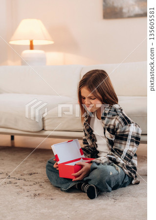 Gift box in hands, birthday. Cute little girl is in the domestic room alone Gift box in hands, birthday. Cute little girl is in the domestic room alone 135605581