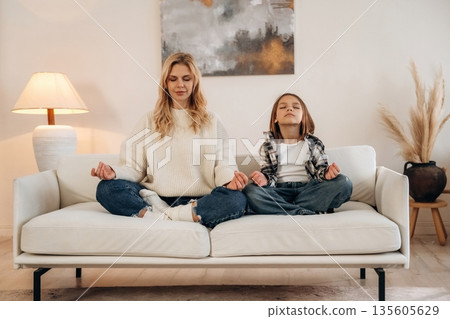 Meditation time, sitting on the sofa. Mother and daughter are together in domestic room Meditation time, sitting on the sofa. Mother and daughter are together in domestic room 135605629