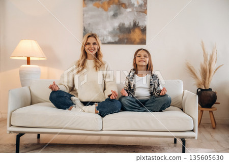 Meditation time, sitting on the sofa. Mother and daughter are together in domestic room Meditation time, sitting on the sofa. Mother and daughter are together in domestic room 135605630