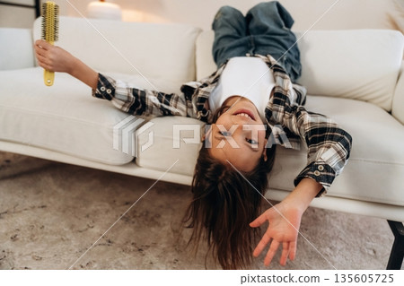 Upside down, lying down on the sofa. Cute little girl is in the domestic room alone Upside down, lying down on the sofa. Cute little girl is in the domestic room alone 135605725