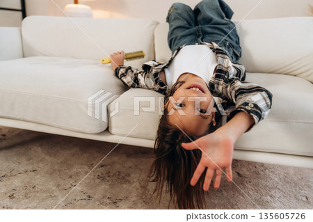 Upside down, lying down on the sofa. Cute little girl is in the domestic room alone Upside down, lying down on the sofa. Cute little girl is in the domestic room alone 135605726