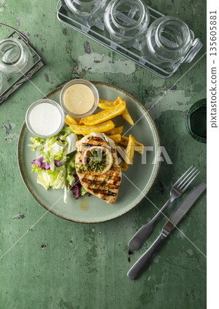 Grilled chicken meal with fries, fresh salad and sauces on green table Grilled chicken meal with fries, fresh salad and sauces on green table 135605881