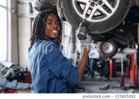 Tire needs to be changed. Male mechanic is with car in garage Tire needs to be changed. Male mechanic is with car in garage 135605892