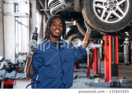 Tire needs to be changed. Male mechanic is with car in garage 135605893