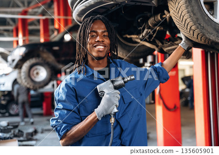Vehicle is high up, about to change the tire. Male mechanic is with car in garage Vehicle is high up, about to change the tire. Male mechanic is with car in garage 135605901