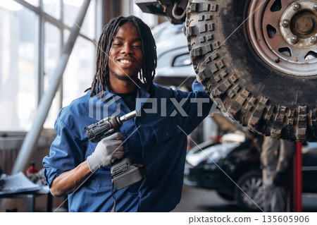 Automatic screwdriver in hand. Male mechanic is with car in garage Automatic screwdriver in hand. Male mechanic is with car in garage 135605906