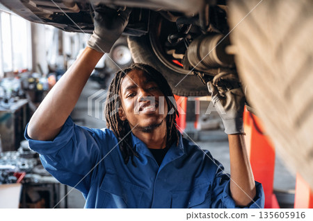 Under the vehicle, fixing it. Male mechanic is with car in garage 135605916