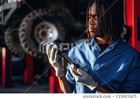 Automobile part in hands. Male mechanic is with car in garage Automobile part in hands. Male mechanic is with car in garage 135605925