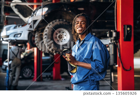 Dreadlocks hairstyle, in blue uniform. Male mechanic is with car in garage 135605926