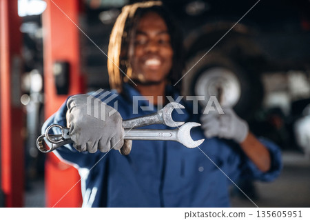 Two wrenches in hand. Male mechanic is with car in garage 135605951