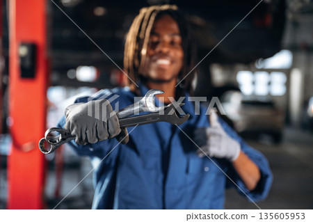 Two wrenches in hand. Male mechanic is with car in garage Two wrenches in hand. Male mechanic is with car in garage 135605953