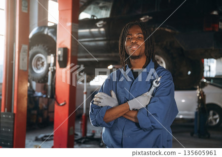 Positive facial expression, holding wrenches. Male mechanic is with car in garage 135605961