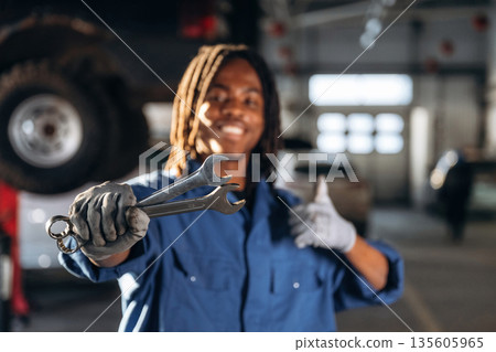 Positive facial expression, holding wrenches. Male mechanic is with car in garage Positive facial expression, holding wrenches. Male mechanic is with car in garage 135605965