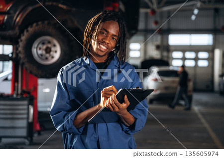 Taking notes into notepad. Male mechanic is with car in garage Taking notes into notepad. Male mechanic is with car in garage 135605974