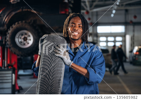 Time to move and change tire. Male mechanic is with car in garage Time to move and change tire. Male mechanic is with car in garage 135605982