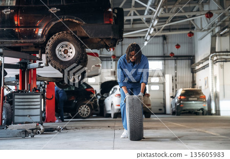 Time to move and change tire. Male mechanic is with car in garage Time to move and change tire. Male mechanic is with car in garage 135605983