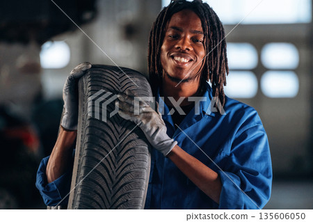 Heavy tire, holding it, changing. Male mechanic is with car in garage Heavy tire, holding it, changing. Male mechanic is with car in garage 135606050