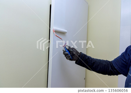 Painter is using roller brush to apply paint on wall in room wall has smooth surface. 135606056