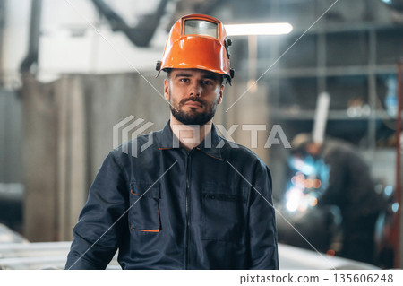 Against blurred background. Welder is standing in protective hat. Man is working in the factory 135606248
