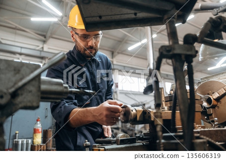 Yellow hardhat, standing by machine. Man is working in the factory Yellow hardhat, standing by machine. Man is working in the factory 135606319