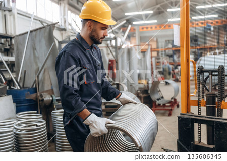 Side view, holding rounded metal product. Man is working in the factory Side view, holding rounded metal product. Man is working in the factory 135606345