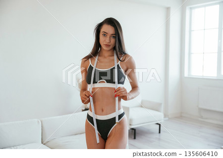 Diet conception, measuring tape. Young woman with slim body type is indoors Diet conception, measuring tape. Young woman with slim body type is indoors 135606410