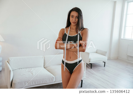 Diet conception, measuring tape. Young woman with slim body type is indoors Diet conception, measuring tape. Young woman with slim body type is indoors 135606412