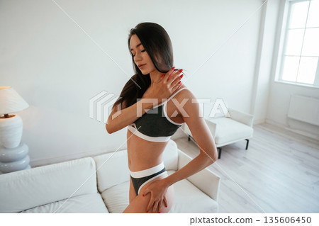 Doing massage by pink roller. Young woman with slim body type is indoors Doing massage by pink roller. Young woman with slim body type is indoors 135606450