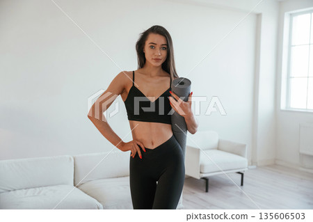 Ready for the yoga, holding mat. Young woman with slim body type is indoors Ready for the yoga, holding mat. Young woman with slim body type is indoors 135606503