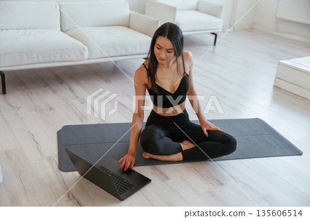 Laptop is on floor, yoga session. Young woman with slim body type is indoors Laptop is on floor, yoga session. Young woman with slim body type is indoors 135606514