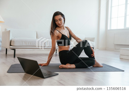 Laptop is on floor, yoga session. Young woman with slim body type is indoors 135606516