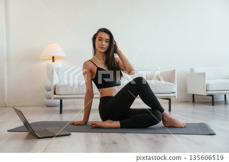 Looking at camera, with laptop on ground. Young woman with slim body type is indoors 135606519