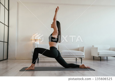 Asana on the yoga mat, with hands up. Young woman with slim body type is indoors Asana on the yoga mat, with hands up. Young woman with slim body type is indoors 135606525