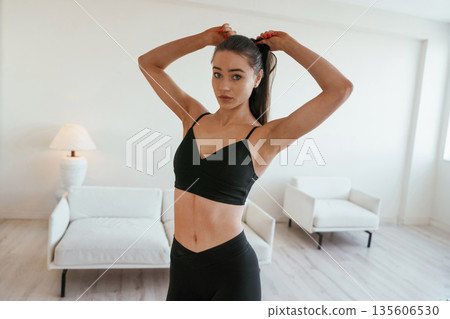 Getting ready for exercises, making ponytail. Young woman with slim body type is indoors Getting ready for exercises, making ponytail. Young woman with slim body type is indoors 135606530