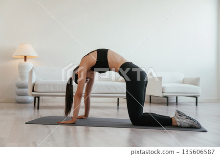 Spine stretching exercise. Young woman with slim body type is indoors Spine stretching exercise. Young woman with slim body type is indoors 135606587