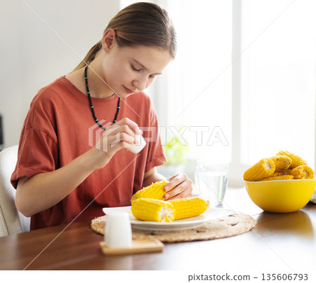 Young Girl Salting Boiling Corn Cobs For Eating In The Kitchen 135606793