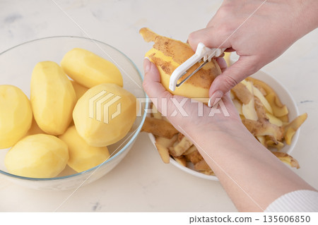 Hands of a woman housewife peeling raw potato with a special tool knife close up, top view Hands of a woman housewife peeling raw potato with a special tool knife close up, top view 135606850