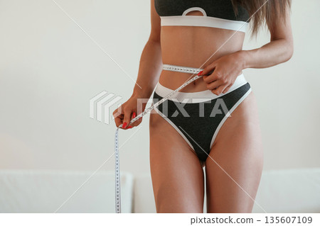 Results of diet and fitness, measuring the waist. Young woman with slim body type is indoors 135607109