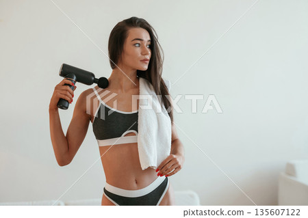 Process of doing self massage using massager. Young woman with slim body type is indoors Process of doing self massage using massager. Young woman with slim body type is indoors 135607122