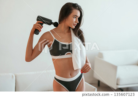 Process of doing self massage using massager. Young woman with slim body type is indoors Process of doing self massage using massager. Young woman with slim body type is indoors 135607123
