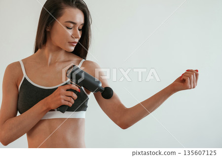 Process of doing self massage using massager. Young woman with slim body type is indoors Process of doing self massage using massager. Young woman with slim body type is indoors 135607125