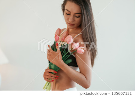 Gift of flowers in hands. Young woman with slim body type is indoors Gift of flowers in hands. Young woman with slim body type is indoors 135607131