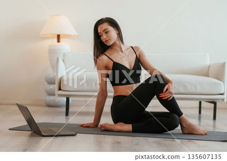 By the laptop on floor. Young woman with slim body type is indoors By the laptop on floor. Young woman with slim body type is indoors 135607135
