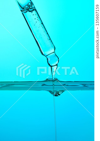 Dropper dispensing liquid into blue water surface Dropper dispensing liquid into blue water surface 135607159