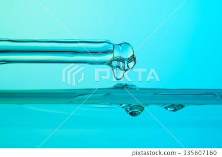 Pipette dripping blue liquid into water surface Pipette dripping blue liquid into water surface 135607160