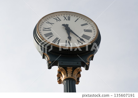 Street clock. Vintage clock in the street. Big street watch against sky. Street clock on a pole. Old small town clock against sky. Time and punctuality. Vintage urban town watch 135607191