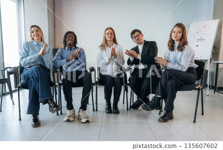 Sitting and applauding. Group of young business people are in conference room Sitting and applauding. Group of young business people are in conference room 135607602