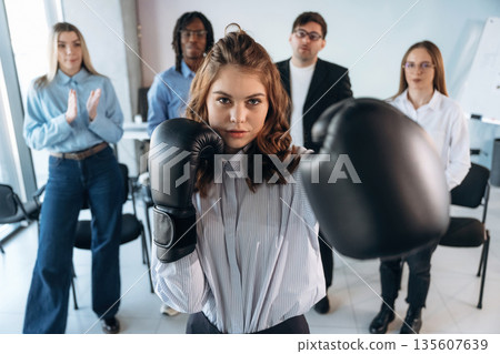 Having fun with boxing gloves. Group of young business people are in conference room Having fun with boxing gloves. Group of young business people are in conference room 135607639