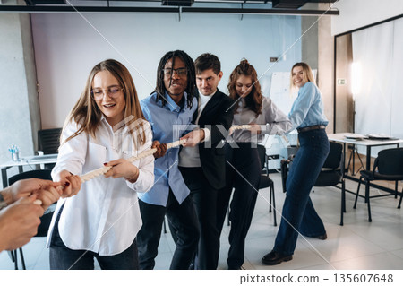 Tug of war game. Group of young business people are in conference room 135607648