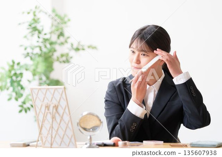 一位穿著招募套裝的女士正在照鏡子,用梳子整理瀏海,檢查自己的儀容。 一位穿著招募套裝的女士正在照鏡子,用梳子整理瀏海,檢查自己的儀容。 135607938